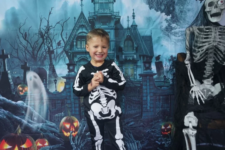 A young boy dressed as a spooky vampire for Halloween, posing confidently with a playful smirk, set against a dimly lit outdoor background.