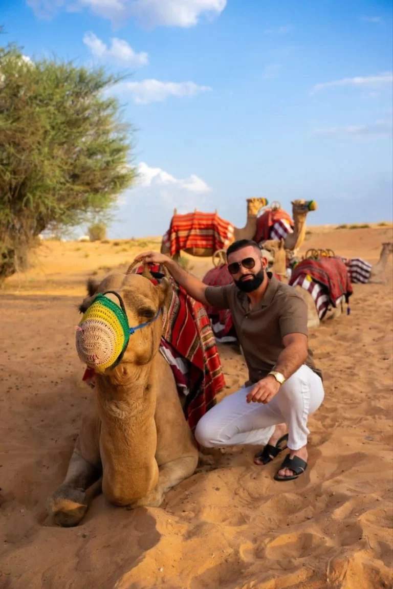 Tourist sitting beside a camel in the sand, enjoying a peaceful moment in the desert.